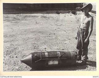 PALMALMAL PLANTATION, JACQUINOT BAY, NEW BRITAIN, 1945-07-13. PRIVATE K. WILSON, HEADQUARTERS 31 SUPPLY DEPOT COMPANY, STANDING BESIDE A COMPLETED "STORPEDO" CONTAINER CONTAINING AUSTRALIA COMFORTS ..