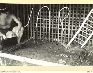 NEW GUINEA. 1944-04-04. VX101554 SIGNALMAN O. LEYDON (1), DISPLAYING JAPANESE SOUVENIRS BY THE SIGN AT THE JAP LADDER SIGNAL CAMP. THE CAMP, UNDER THE CONTROL OF THE 23RD LINE SECTION, 18TH LINES ..