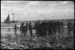 Group of people at the shore, with ship in the background