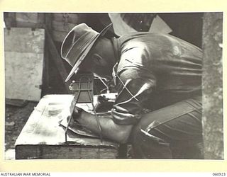 NEW GUINEA. 1943-11-28. VX133 BRIGADIER S. H. W. C. PORTER, DSO, ED, COMMANDING 24TH AUSTRALIAN INFANTRY BRIGADE, STUDYING AERIAL PHOTOGRAPHS THROUGH A STEREOSCOPE