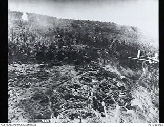 Boram, Wewak, New Guinea. 1944-10-16. Aerial photograph of a Mitchell B25 bomber aircraft of the United States Army Air Force dropping bombs over Japanese anti-aircraft positions on the ridge near ..