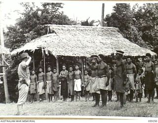 BUGENG, NEW GUINEA, 1943-10-21. NX155085 CAPTAIN R.G. ORMSBY OF THE AUSTRALIAN AND NEW GUINEA ADMINISTRATIVE UNIT BEING SALUTED BY THE "ZULUAI" AND THE "TUL-TULS" OF THE VILLAGE