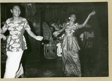 The picture depicts two women performing a dance. In the background, uniform-dressed men are seen as spectators. The picture is taken in Samoa in connection with the mine ship Älvsnabens long voyage 1966-1967.