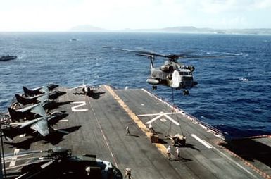 AV-8 Harrier aircraft line the deck as a CH-53 Sea Stallion helicopter prepares to lift a howitzer from the amphibious assault ship USS SAIPAN (LHA-2) during Fleet Ex 1-90