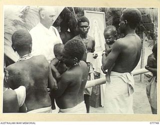 BOUGAINVILLE ISLAND. 1944-12-24. QX42695 CHAPLAIN J.P. MCMANUS (RC) 2/ 1ST AUSTRALIAN GENERAL HOSPITAL, ASSISTED BY THE CATECHIST, NABUAI, CHRISTENING NATIVE BABIES IN THE AUSTRALIAN NEW GUINEA ..