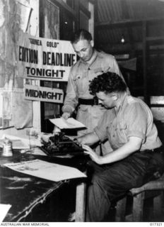 New Guinea. 1944. Major R. B. Leonard of Melbourne, Vic (standing), and Lieutenant J. D. Holdsworth of Sydney, NSW, editorial staff of "Guinea Gold" the newspaper which is distributed daily to ..