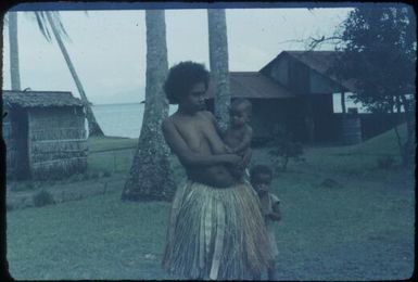 Native woman in grass skirt with two young children : Mapamoiwa Station, D'Entrecasteaux Islands, Papua New Guinea, 1956-1959 / Terence and Margaret Spencer