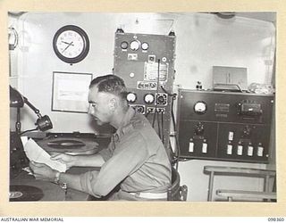 WEWAK, NEW GUINEA. 1945-10-29. SERGEANT E.C. PARRENT, 1 BROADCASTING STATION, AUSTRALIAN ARMY AMENITIES SERVICE, AT THE MICROPHONE OF RADIO STATION 9AJ ANNOUNCING RECORDS