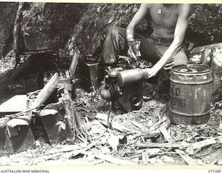 BOUGAINVILLE ISLAND. 1944-11-25. NX153286 SIGNALLER E.R. BOWDEN, 7TH INFANTRY BRIGADE SIGNALS ATTACHED TO 9TH INFANTRY BATTALION REFUELLING A BATTERY CHARGER AT BATTALION HEADQUARTERS