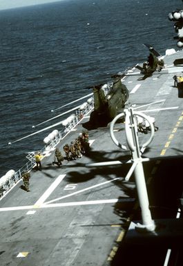 A squad of Marines aboard the amphibious assault ship USS SAIPAN (LH-2) are being directed to board a Marine CH-46 Sea Knight helicopter, not shown. Behind them is another CH-46 and a Marine AH-1 Sea Cobra helicopter