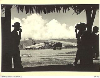 LAE, NEW GUINEA, 1944-03-29. THE LAE AIRSTRIP VIEWED FROM THE YOUNG MEN'S CHRISTIAN ASSOCIATION, WHERE FREE COFFEE IS PROVIDED TO SOLDIERS TRAVELLING BY PLANE. DOUGLAS TRANSPORT AIRCRAFT OF THE ..
