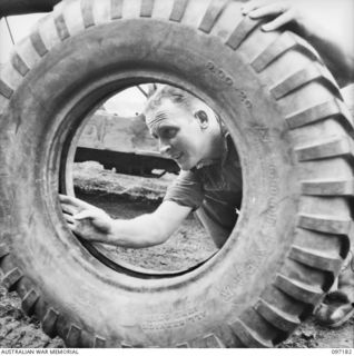 CAPE WOM, NEW GUINEA. 1945-09-27. CORPORAL J.D. IREDALE, 110 BRIGADE ORDNANCE FIELD PARK, INSPECTING A TYRE FOR IMPERFECTIONS