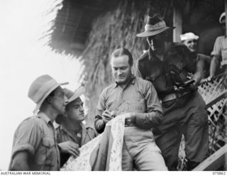 Bob Hope, famous American comedian, and leader of the Bob Hope concert party, which is touring the northern battle areas entertaining the troops, autographing a captured Japanese flag for a member ..