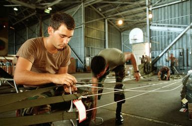 A1C Donald Popp, 8th Mobile Aerial Port Squadron, repairs suspension lines on parachute prior to attaching packages to be delivered during Christmas Drop. The annual airdrop is a humanitarian effort providing aid to needy islanders throughout Micronesia during the holiday season