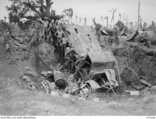 HANSA BAY, NEW GUINEA. 1944-06-22. TROOPS OF THE 8TH FIELD COMPANY, EXAMINING AN ENEMY TRUCK AND EQUIPMENT DUMPED IN A LARGE BOMB CRATER BY THE RETREATING JAPANESE FORCES