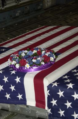 A wreath sits on top of transfer cases draped in American Flags on board a C-17 Globemaster cargo aircraft at Andersen Air Force Base (AFB), Guam