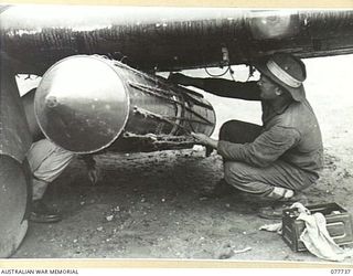 BOUGAINVILLE ISLAND. 1944-12-25. GROUND STAFF PERSONNEL OF NO.5 TACTICAL RECONNAISSANCE SQUADRON RAAF, FITTING A "STOREPEDO" CONTAINING AN AUSTER AIRCRAFT PROPELLER TO THE BOMB RACKS OF A ..