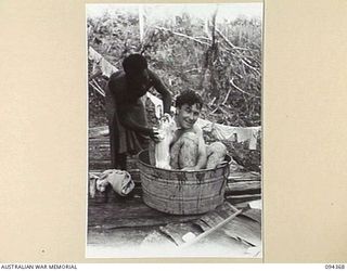 YAMIL 2, NEW GUINEA. 1945-07-20. SERGEANT N.H. KELLY, ARMY PUBLIC RELATIONS REPRESENTATIVE IN THE SECTOR (2) HAVING A HOT BATH IN A TUB AND HIS BACK SCRUBBED BY A WASH-BOY FROM THE MAIN DRESSING ..