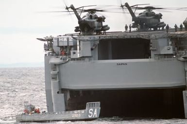 An LCM 6 mechanized landing craft is piloted past the docking well of the amphibious assault ship USS SAIPAN (LHA 2) during NATO Exercise NORTHERN WEDDING 86. Two CH-53E Super Stallion helicopters are on the flight deck