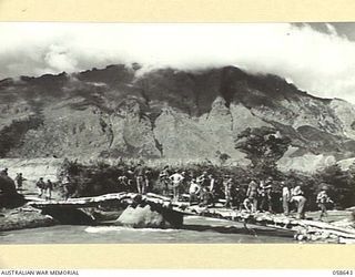 GUSAP RIVER, NEW GUINEA, 1943-10-04. TROOPS OF THE 2/6TH AUSTRALIAN FIELD COMPANY, ROYAL AUSTRALIAN ENGINEERS WORKING TO COMPLETE A BRIDGE, AS TROOPS OF THE 2/14TH AUSTRALIAN INFANTRY BATTALION ..