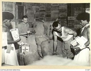 1942-12-17. NEW GUINEA. RED CROSS. CORPORAL T.R. WALKER MELBOURNE, AND PTE. C.A. MAGEE OF BRISBANE ARE ASSISTED BY TWO NATIVES TO PACK RED CROSS SUPPLIES WHICH ARE TO BE DROPPED TO TROOPS IN ..