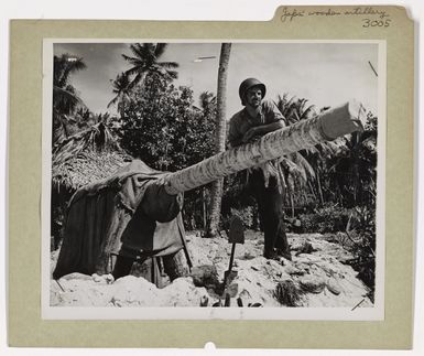 Photograph of Coast Guardsman Leaning on Dummy Japanese Artillery