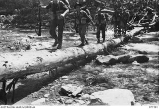 BOUGAINVILLE ISLAND. 1944-11-25. TROOPS OF A COMPANY, 9TH INFANTRY BATTALION CROSSING A LOG BRIDGE OVER THE LARUMA RIVER NEAR THE BATTALION HEADQUARTERS AS THEY MOVE FORWARD TO TAKE OVER THE FRONT ..