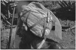 Man wears fabric and ribbon headdress with kinship chart pinned to it