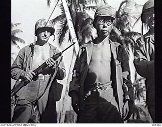 GUAM. C.1945. A JAPANESE PRISONER OF WAR WAITS FOR INTERROGATION BY INTELLIGENCE OFFICERS. HE IS CLOSELY GUARDED BY A US MARINE ARMED WITH AN M1 CARBINE. (NAVAL HISTORICAL COLLECTION)
