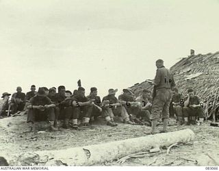 BABIANG, NEW GUINEA. 1944-11-07. CHAPLAIN W.M. ROOKE, (CHURCH OF ENGLAND) (1A),OF REGIMENTAL HQ 2/6 COMMANDO SQUADRON WITH MEMBERS OF 2/10 CDO SQN CONDUCTING AN IMPROMPTU CHURCH PARADE BEFORE A ..