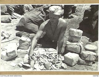 DUMPU, NEW GUINEA, 1943-10-10. NX100193 PRIVATE J.E. WATERWORTH OF THE 7TH AUSTRALIAN DIVISION POSTAL UNIT SPREADS ON THE GROUND THE WRECKAGE OF AN IMPROPERLY PACKED PARCEL