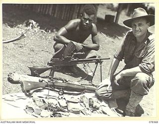 TAMKAIDAN, NEW BRITAIN. 1945-01-15. QX4869 LIEUTENANT J. SAMPSON AND A NATIVE MEMBER OF THE UNIT SHOWING GUERRILLA EQUIPMENT ISSUED TO MEMBERS OF THE ALLIED INTELLIGENCE BUREAU. SEEN ARE:- RIFLE, ..