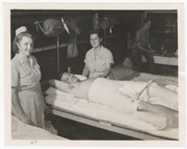 [Nurses tending to wounded serviceman in body cast]