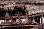An adult surrounded by children sitting at entrance to a house at Kambaram village, Middle Sepik, [Papua New Guinea, 1969?]