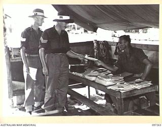 CAPE WOM, NEW GUINEA. 1945-09-29. SERGEANT A.R. MCDOUGALL (1) AND STAFF SERGEANT L.G. FARRAR (2), HANDING IN THEIR REQUEST NUMBERS TO CORPORAL F.R. SAWYER (3), AT RADIO 6 DIVISION, HEADQUARTERS 6 ..