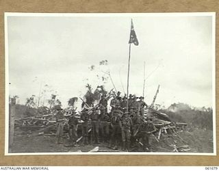 WAREO, NEW GUINEA. 1943-12. GROUP OF OFFICERS AND MEN OF THE 2/23RD AUSTRALIAN INFANTRY BATTALION, AROUND THE UNIT VICTORY FLAG. THIS FLAG WAS PREVIOUSLY RAISED OVER KOKODA, BUNA AND SATTELBERG. ..