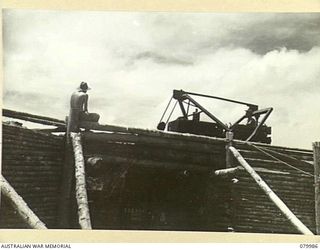 TOKO-BARARA ROAD, BOUGAINVILLE, SOLOMON ISLANDS. 1945-03-28. TROOPS OF THE 15TH FIELD COMPANY, ROYAL AUSTRALIAN ENGINEERS, USE A BULLDOZER TO FILL A TRUCK FROM A "CHINAMAN" CONTAINING TOP DRESSING ..