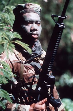 PH1 Ted Salois Tinian, Marianas Islands....Marine PFC. Edwin Childs, his face smeared with camouflage paint, stands in the jungle with his M-16A2 rifle during exercise Kennel Bear '89. PFC. Childs and other Marines from Marine Barracks Guam are acting as aggressors against Seabees from Navy Mobile Construction Battalion 3 and Marines from the 3rd Force Service Support Group. OFFICIAL U.S. NAVY PHOTO (RELEASED)