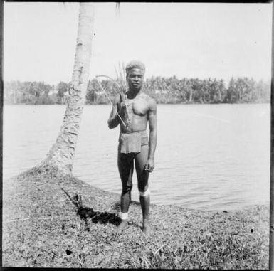 Ramu man standing with bow and arrows over shoulder and a river behind, Ramu River [?], New Guinea, 1935 / Sarah Chinnery