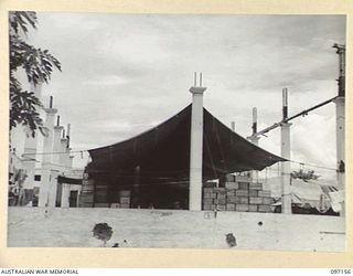 RABAUL, NEW BRITAIN. 1945-09-25. A LARGE TARPAULIN STRETCHED OVER AUSTRALIAN ARMY CANTEENS SERVICE GOODS IN A WRECKED BURNS PHILP STORE