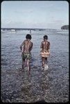 Girls walk in shallow water near coral reef edge near Wawela village