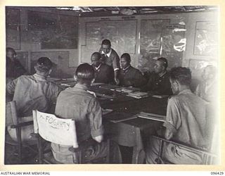 CAPE WOM, NEW GUINEA, 1945-09-13. GENERAL DISCUSSION AT COMMENCEMENT OF A CONFERENCE BETWEEN STAFF OFFICERS OF 6 DIVISION, HEADED BY LIEUTENANT-COLONEL J. BISHOP, GENERAL STAFF OFFICER I, AND STAFF ..