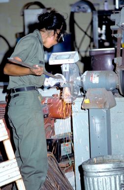 A member of a naval mobile construction battalion uses a grinder to shave down a steel bar