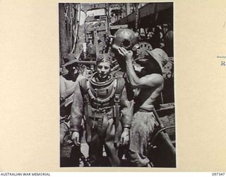 RABAUL, NEW BRITAIN. 1945-09-30. DIVER J. DALLEY BEING RELIEVED OF HIS HELMET AFTER COMING UP FROM HOLD AT THE STERN OF THE JAPANESE TANKER NO. 5301 AFTER INSPECTION. THE VESSEL, WHICH WAS SUNK BY ..