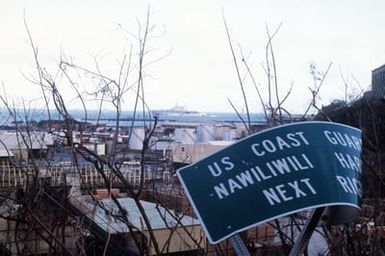A damaged sign in the foreground is a minor example of destruction caused by Hurricane Iniki when it struck the island of Kauai. The amphibious assault ship USS BELLEAU WOOD (LHA-3) is anchored in the harbor, background, as landing craft and helicopters deliver supplies from the vessel to residents of Kauai as part of Joint Task Force Garden Isle, a joint military disaster relief effort