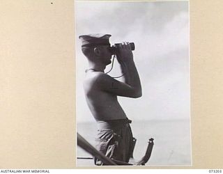 OFF MADANG, NEW GUINEA. 1944-05-14. ABLE SEAMAN M L PHELAN (1), SEARCHES THE SEA AND SKY WITH BINOCULARS WHILE ON LOOKOUT DUTY ABOARD THE RAN FRIGATE HMAS BARCOO. THE VESSEL IS ON ACTIVE PATROL ..