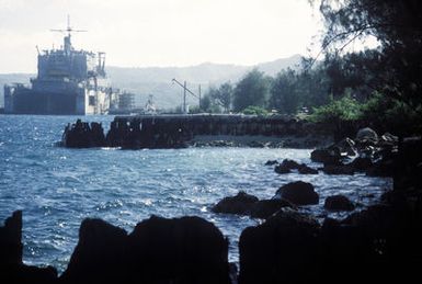 View of a section of the old Japanese refueling piers used during World War II. The piers were later used by the liberating American troops to offload supplies after the liberation of Guam in July 1944. In the background is a Military Sealift Command (MSC) oiler in a floating dry dock. The importance of Naval Station Guam has greatly increased since the closing of Subic Bay Naval Station in the Philippines
