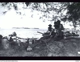 LABUAN, NORTH BORNEO. 11 JUNE 1945. MEMBERS OF TANK ATTACK PLATOON, HQ, 2/43 INFANTRY BATTALION, MANNING A 2-POUNDER GUN POSITION ON BROWN BEACH 2. NOTE ALLIED SHIPPING IN THE HARBOUR WITH PAPUA ..