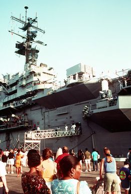 Family and friends watch from the pier as crew members aboard the amphibious assault ship USS GUAM (LPH-9) prepare to depart for the Persian Gulf in response to Iraq's invasion of Kuwait