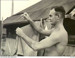 TOROKINA, BOUGAINVILLE ISLAND, SOLOMON ISLANDS . C. 1945-01-16. FLYING OFFICER PERCY BOWYER, MELBOURNE, VIC, FORMER COLLINGWOOD CHAMPION AUSTRALIAN RULES FOOTBALLER, IN A DIFFERENT ROLE AS HE HANGS ..